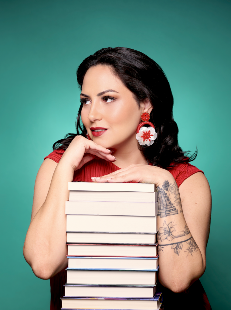 Natalia Hernandez author headshot of the authors hands resting on a stack of books while they look away from the camera.
